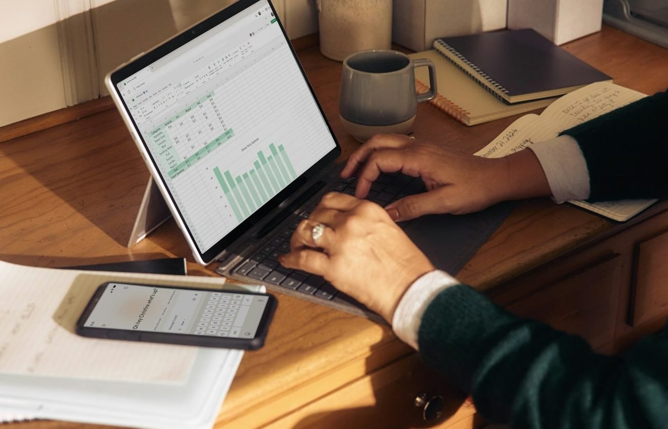 Professional working on a laptop with spreadsheets at a desk